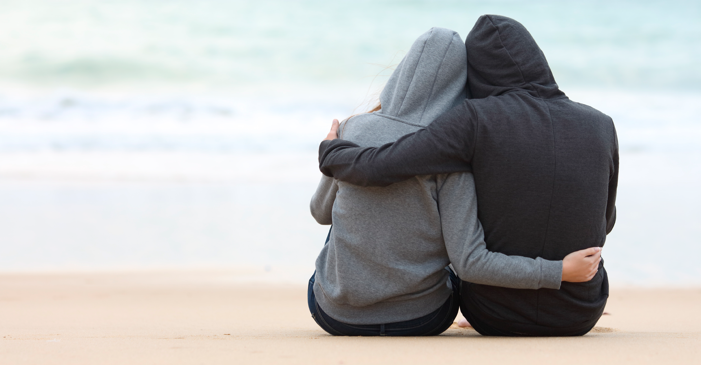 A couple holds each other as they sit on the beach and look out to see.