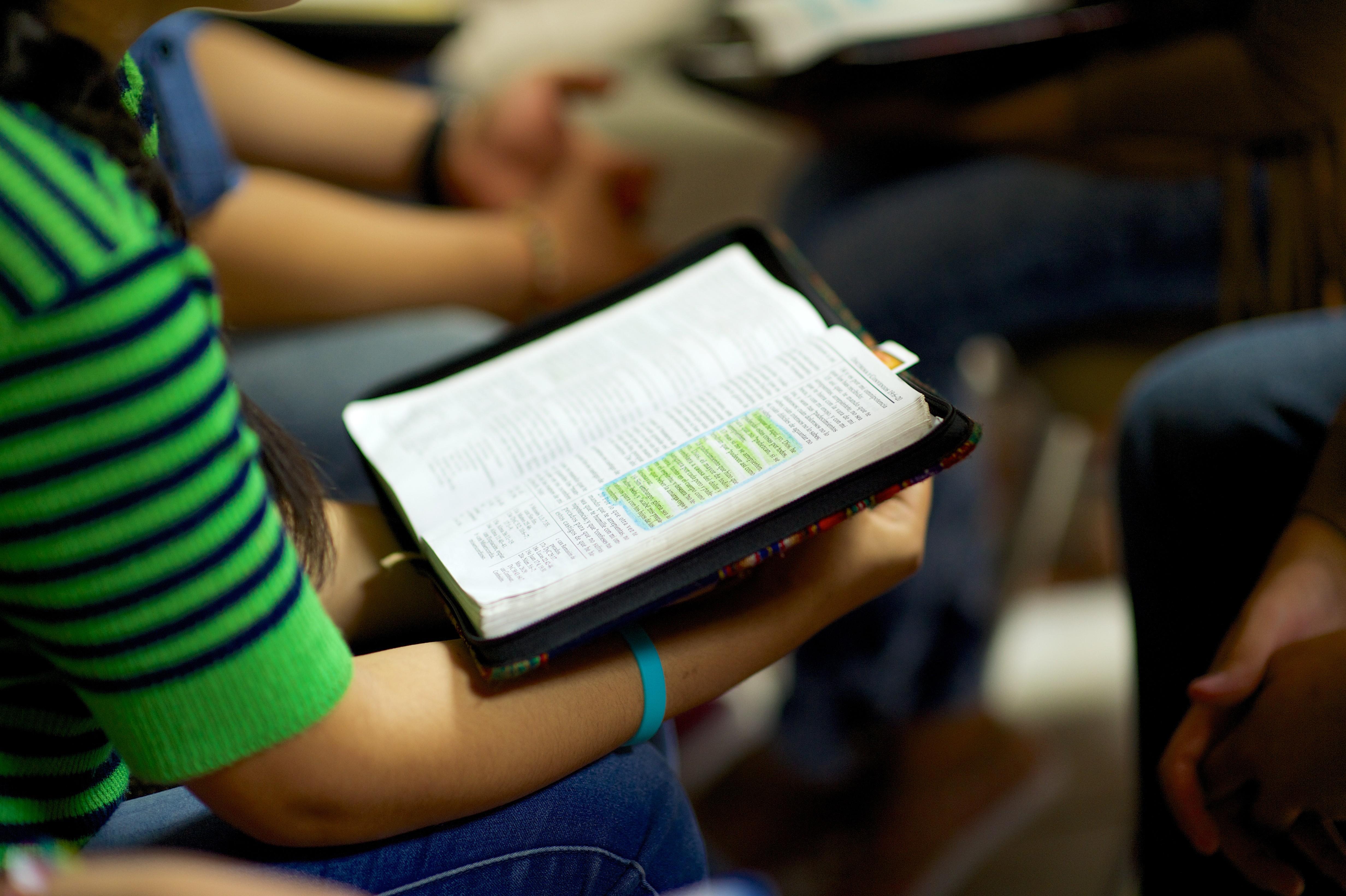 A girl in a green shirt holding open a book of scriptures in a zipper case during a group discussion.