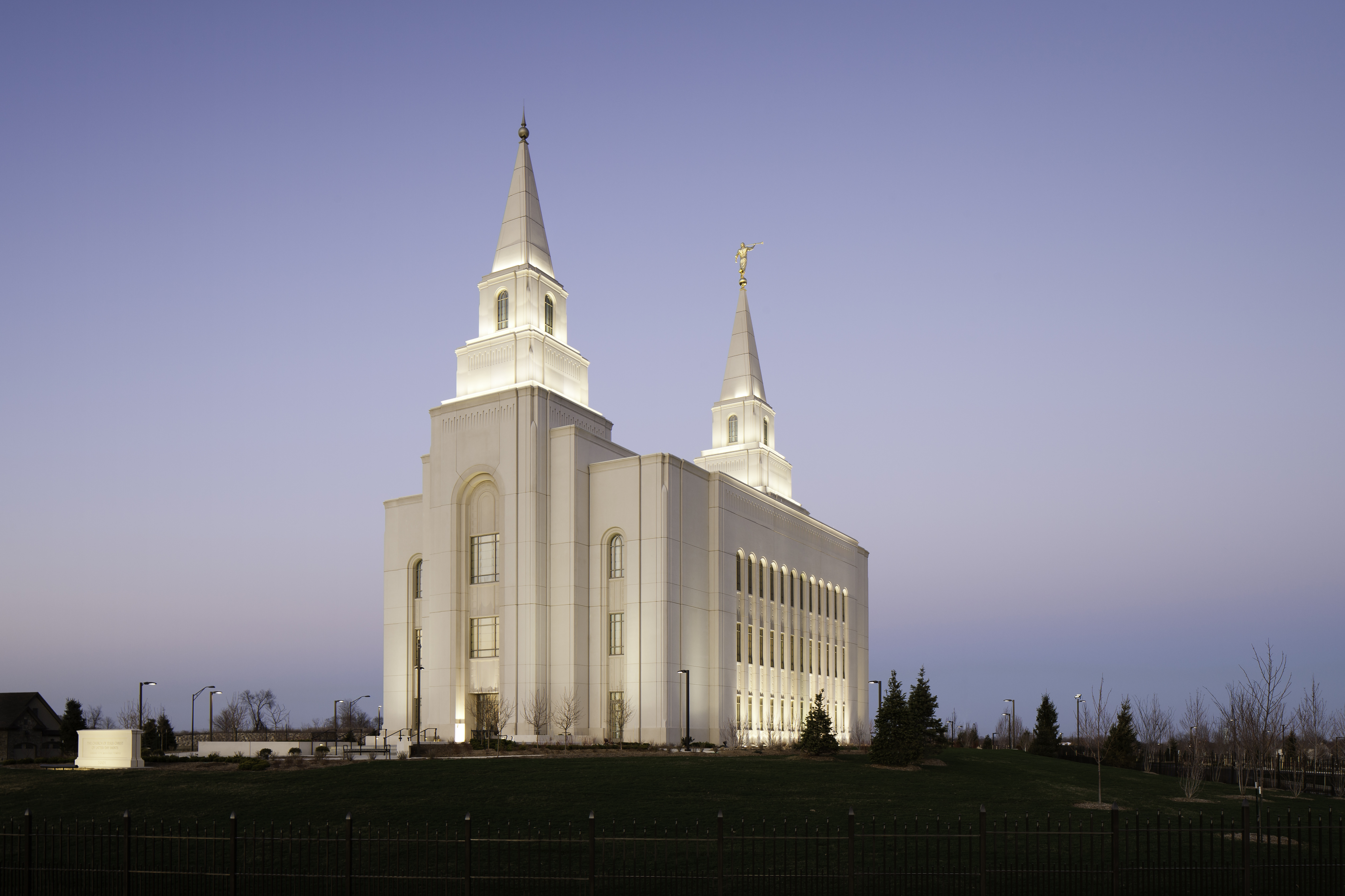 The Kansas City Missouri Temple at night, with the lights illuminating the exterior of the building and a blue sky above.