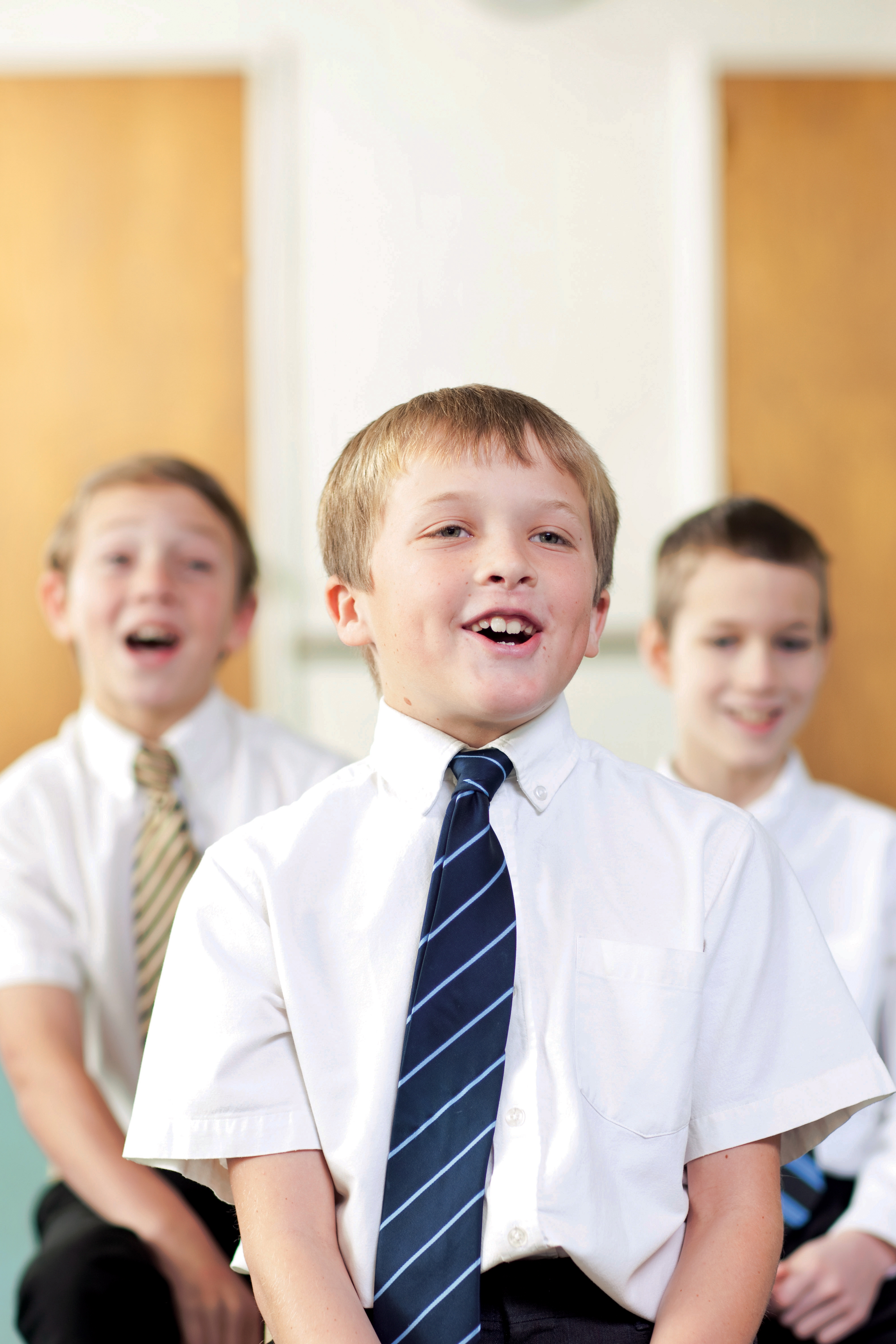 Three Primary-age boys sit in a Primary room in white shirts and ties and sing together during singing time.