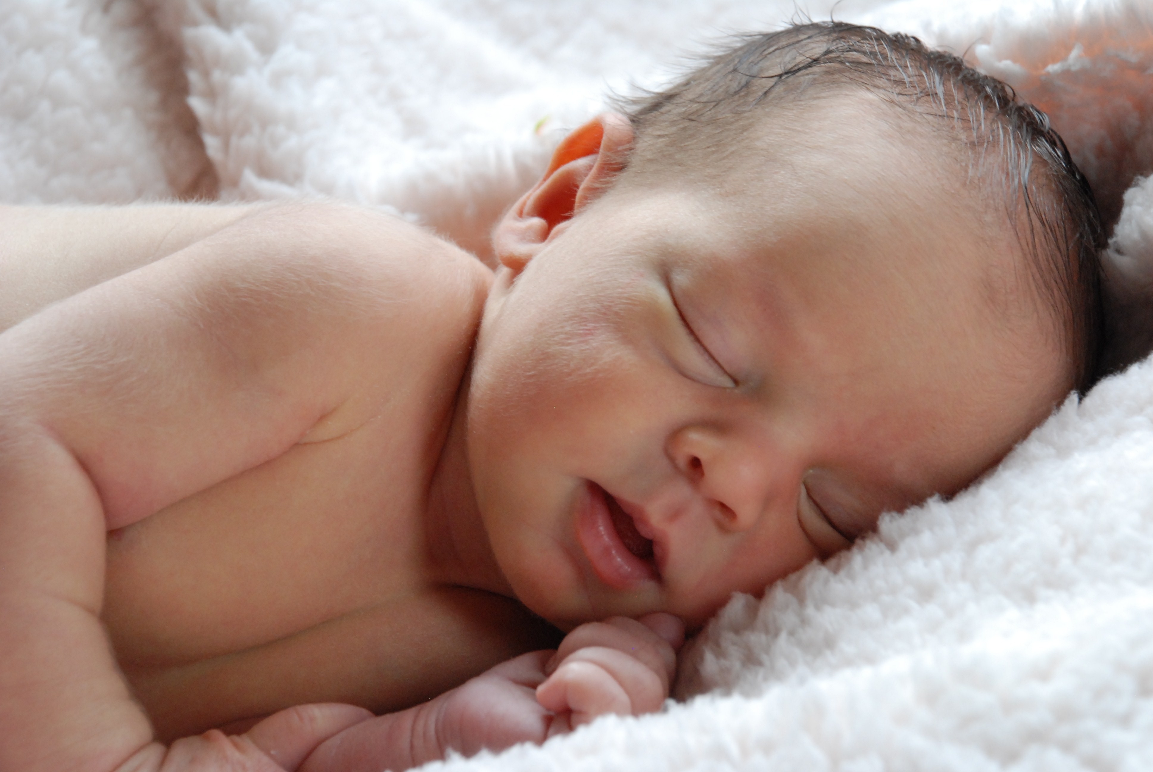 A newborn baby sleeping on a white, fluffy blanket.