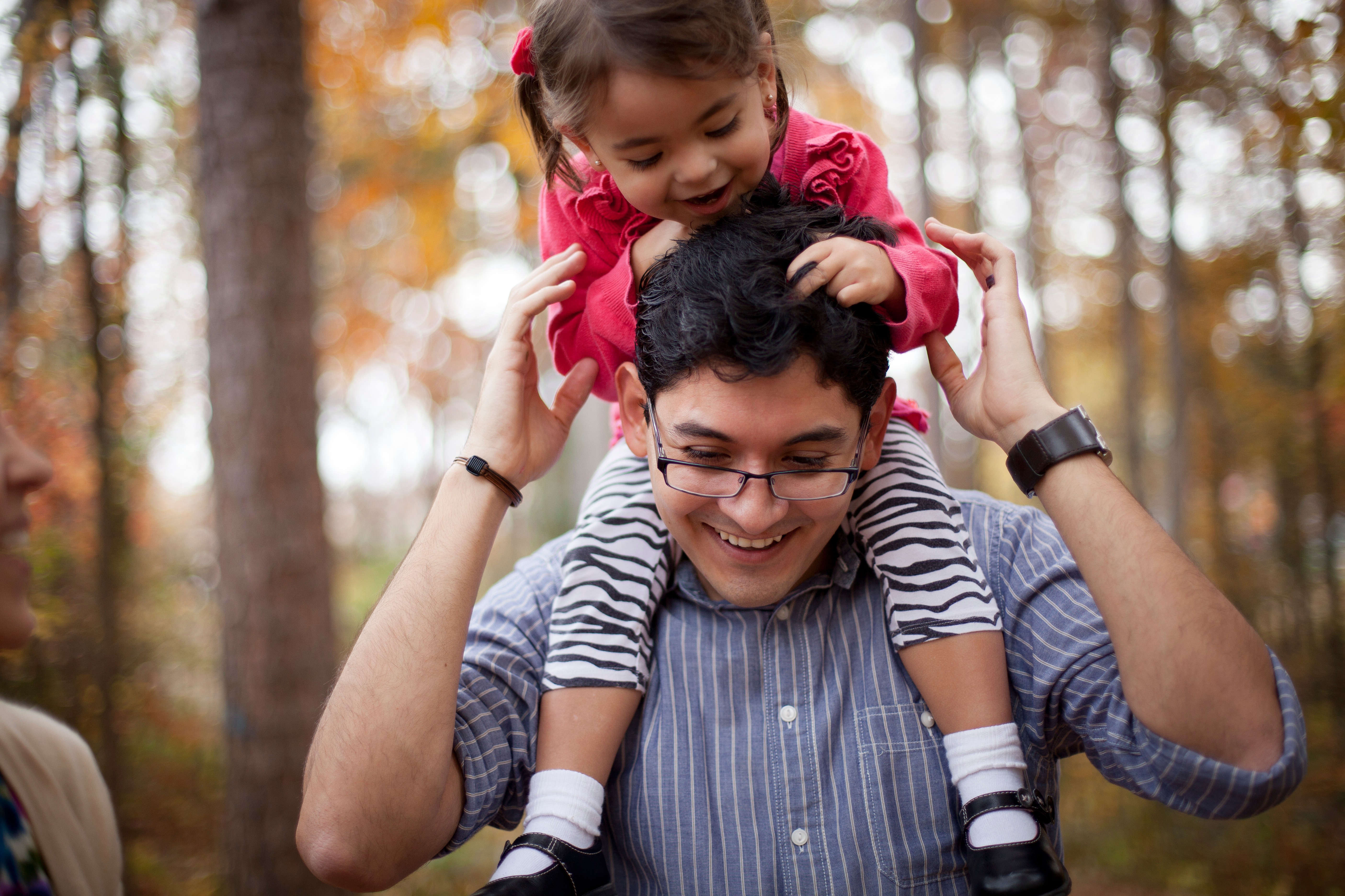 A toddler girl sits on her father’s shoulders and smiles.