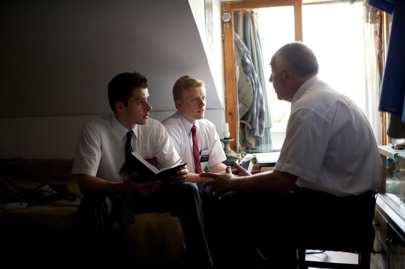 Dos misioneros se sientan con un hombre mayor mientras conversan sobre el evangelio de Jesucristo y la Biblia