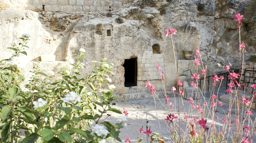 A photo of the Garden Tomb in Jerusalem with pink flowers in the foreground. 