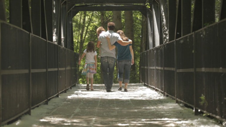 A family walks arm in arm across a covered bridge