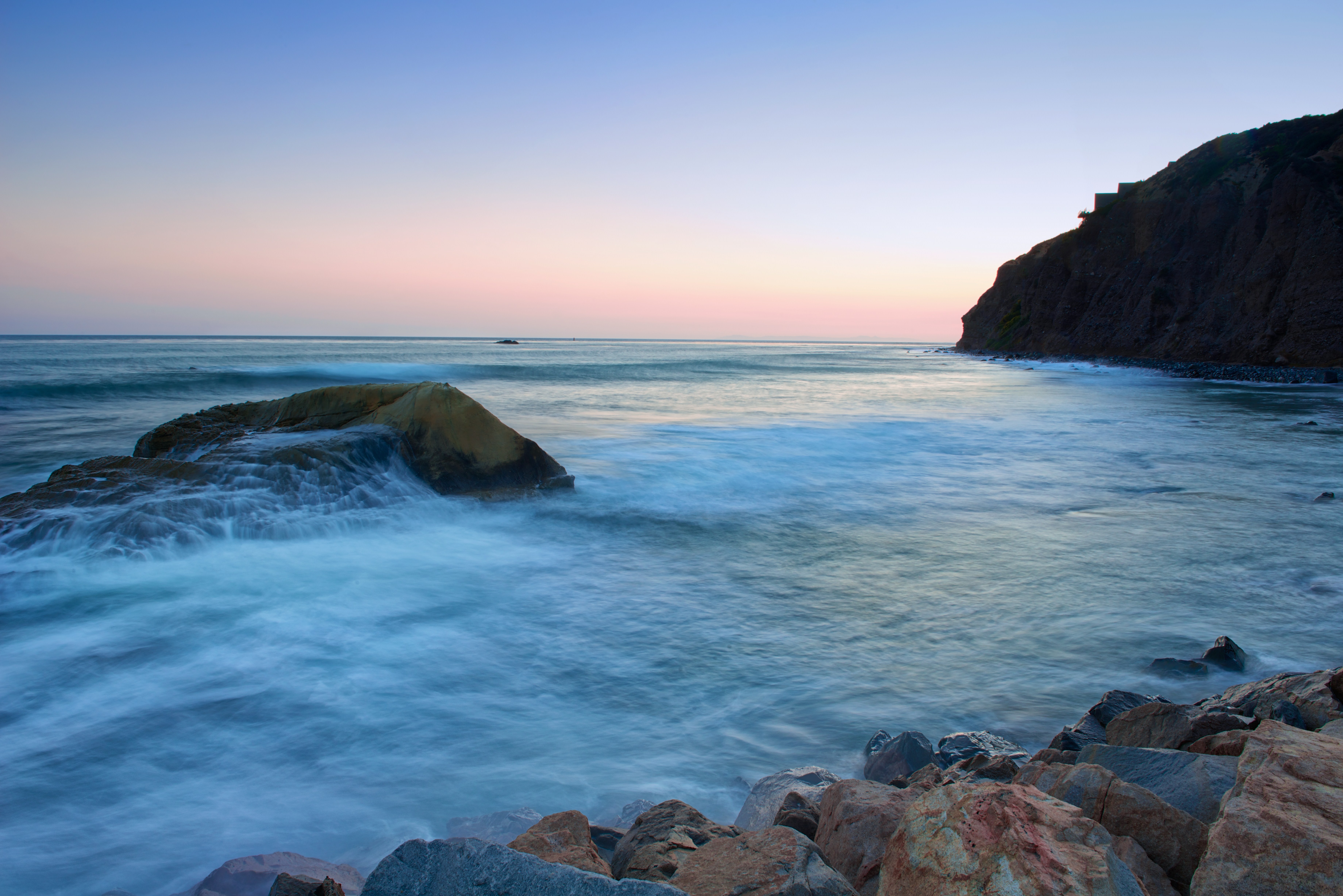 The Pacific Ocean bordered by rocks on the California coastline at dusk.