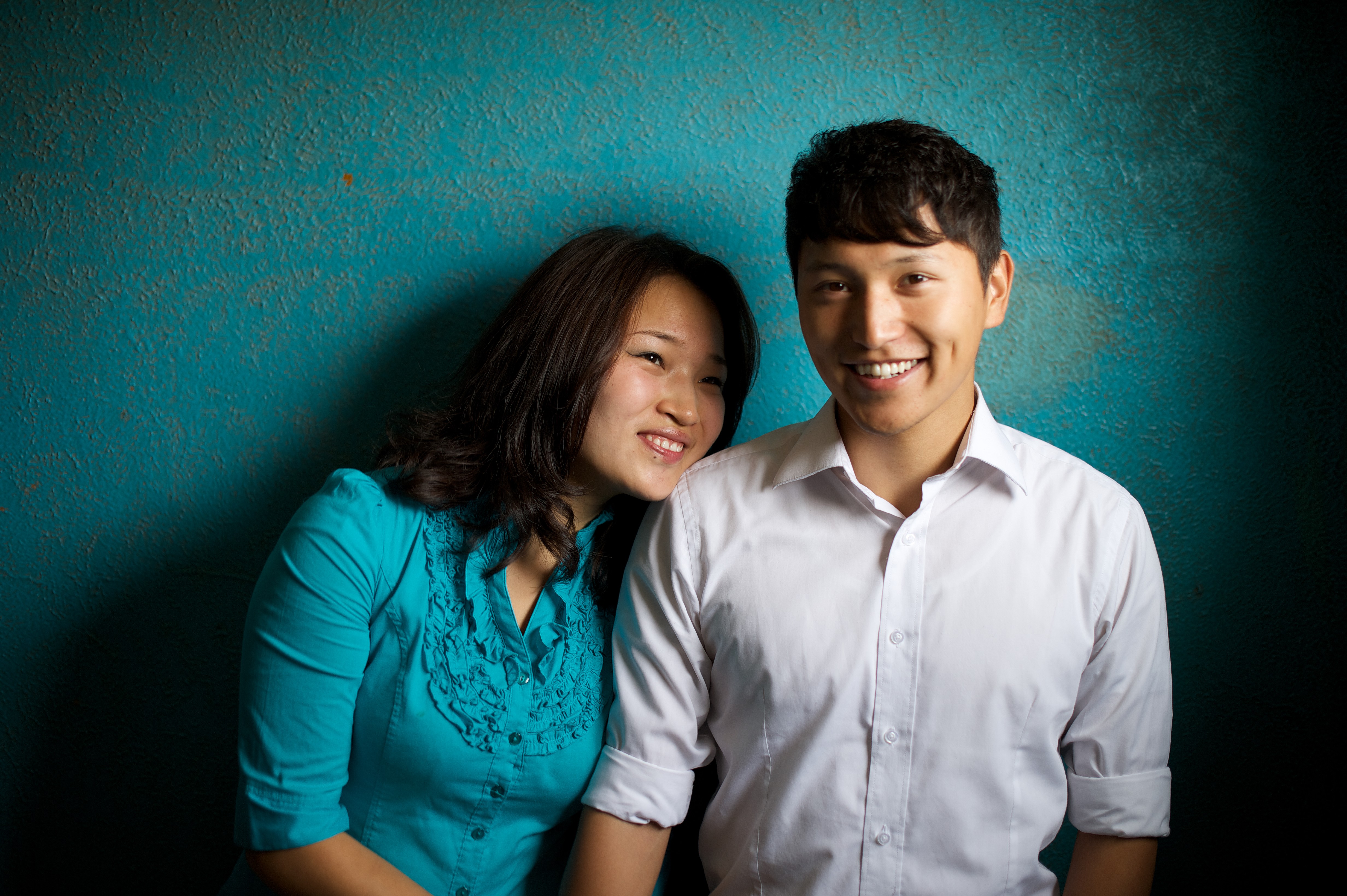 A portrait of a woman in a blue blouse and her husband in a button-up shirt, with a blue background.