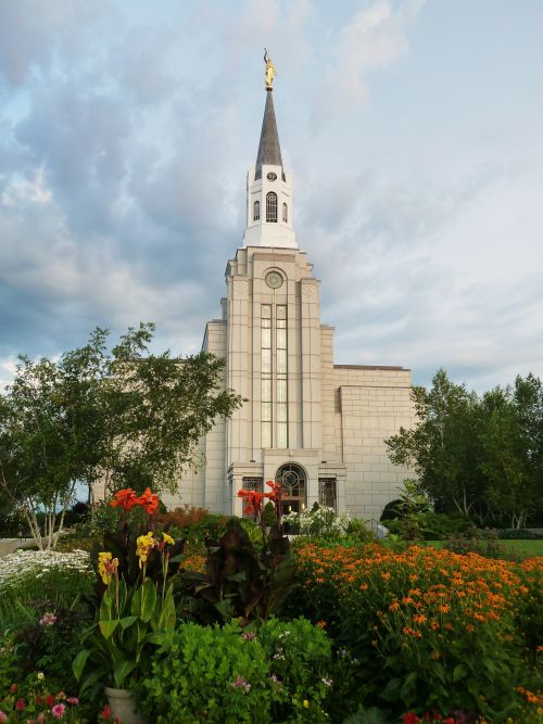A view of the front of the Boston Massachusetts Temple in the summer, with trees and flowers in the foreground.