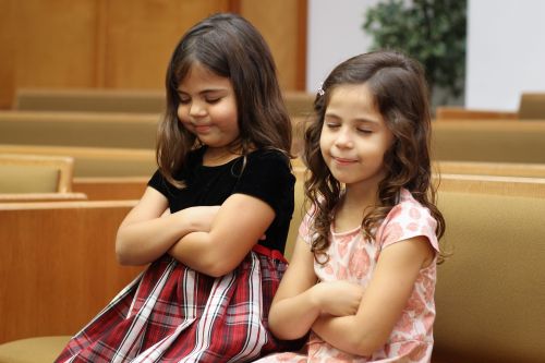 Two girls sitting on chapel bench with folded arms. (horiz)
