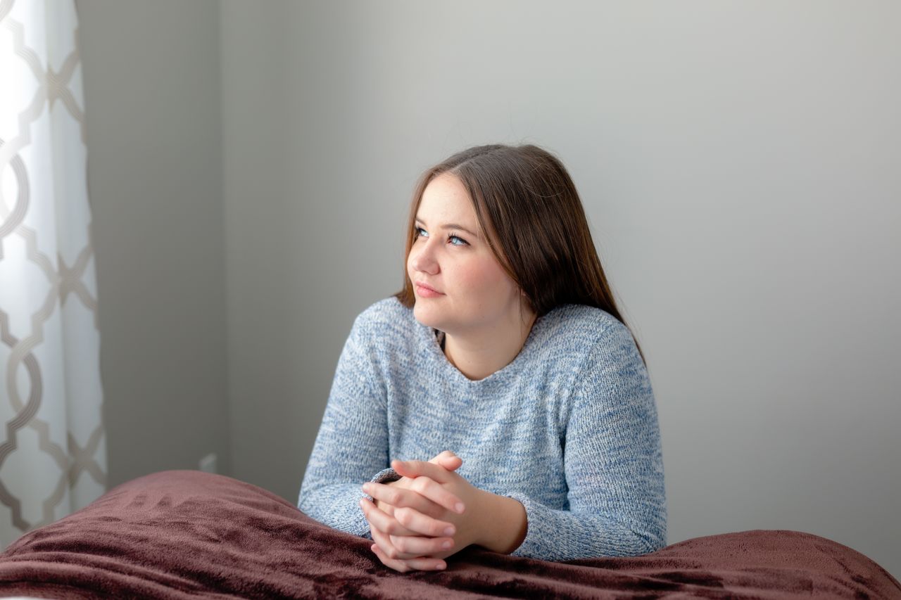 Una mujer joven arrodilla a lado de su cama para orar