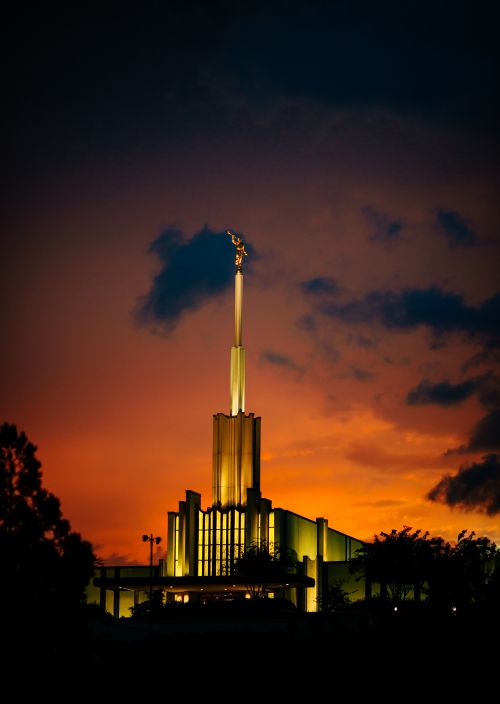 The front of the Atlanta Georgia Temple lit up during sunset, with a deep orange sky in the background.