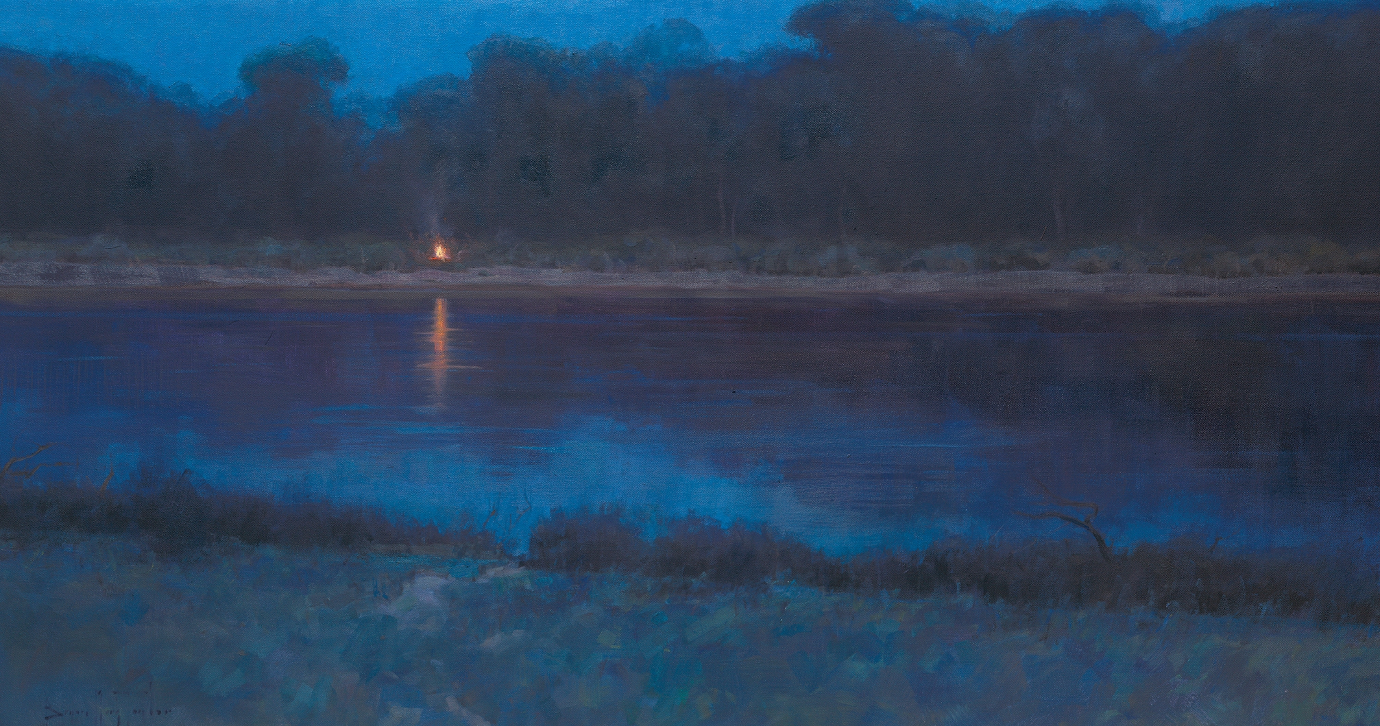 A campfire on the shores of the Missouri River during the evening.  There are trees along the river.
