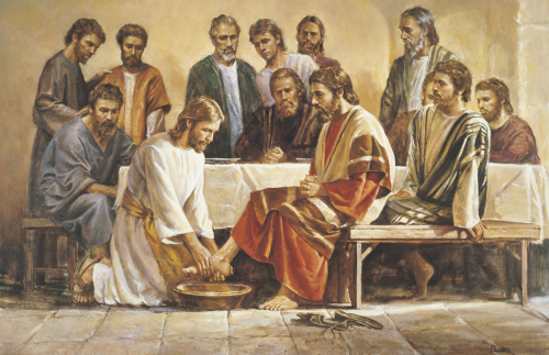 Jesus Christ with the twelve apostles. Christ (depicted wearing a white robe with a yellow sash), is kneeling before one of the apostles as He washes the feet of that apostle. The other eleven apostles are gathered around a table (having just completed the last supper). They are watching Christ. (John 13:1-20)