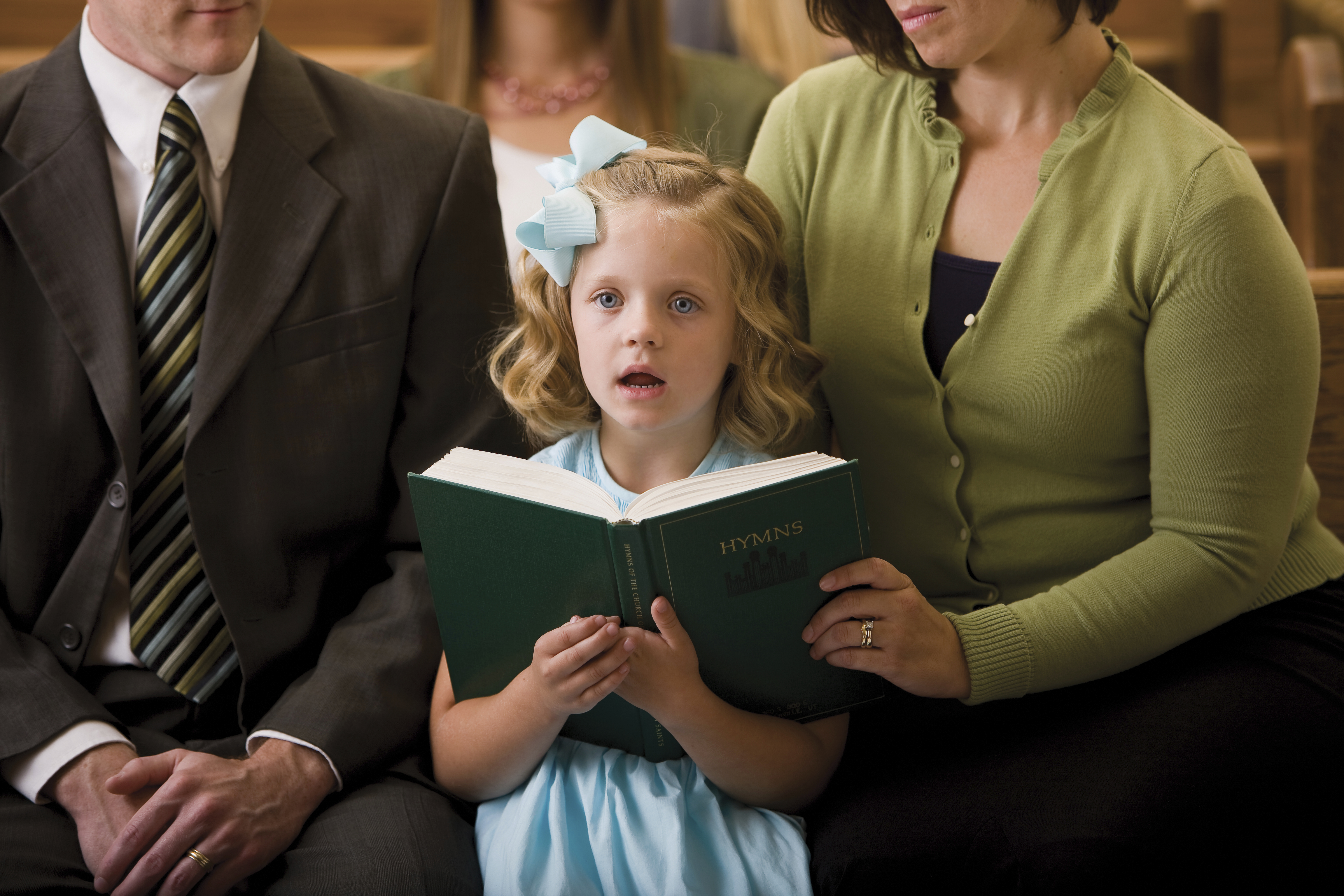 A young girl sings in Church while holding a hymnbook.