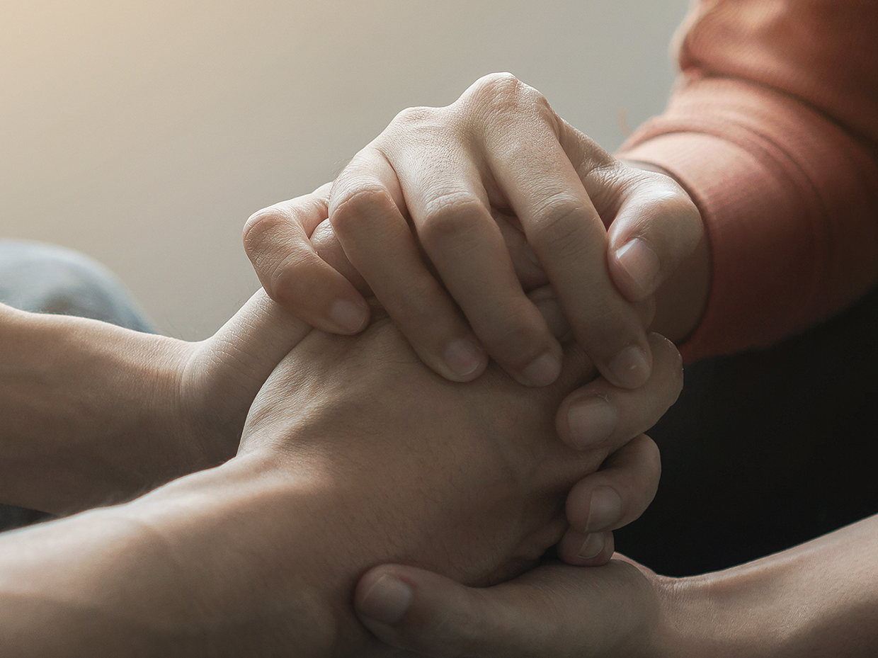 Two people facing each other hold hands as they support each other.